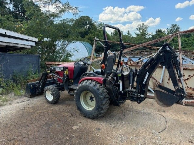 A tractor with a backhoe attached to it is parked in a dirt lot.