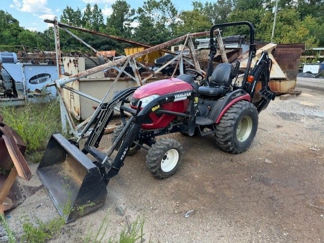 A red tractor with a bucket attached to it is parked in a yard.