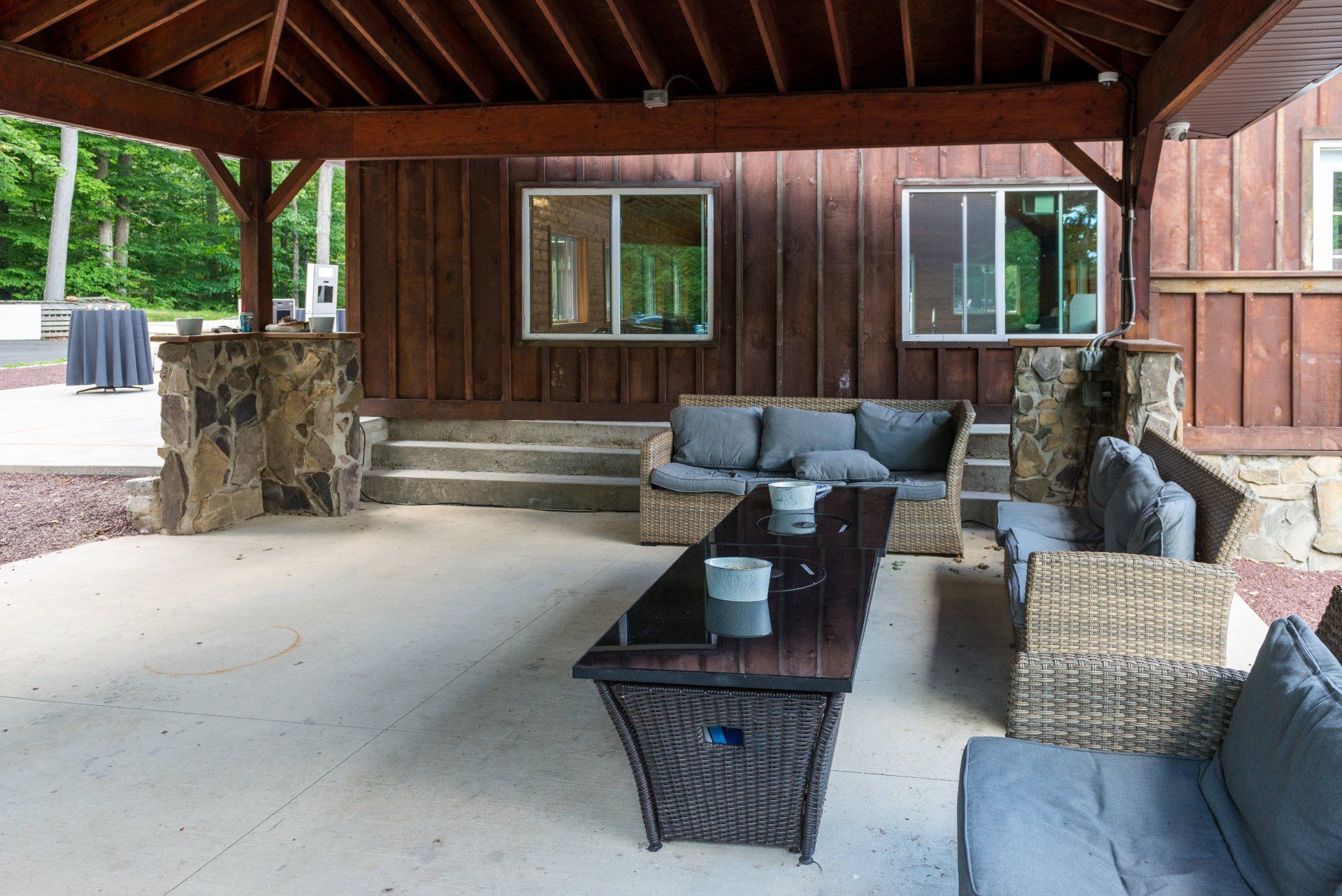 A patio with wicker furniture and a table under a wooden roof.