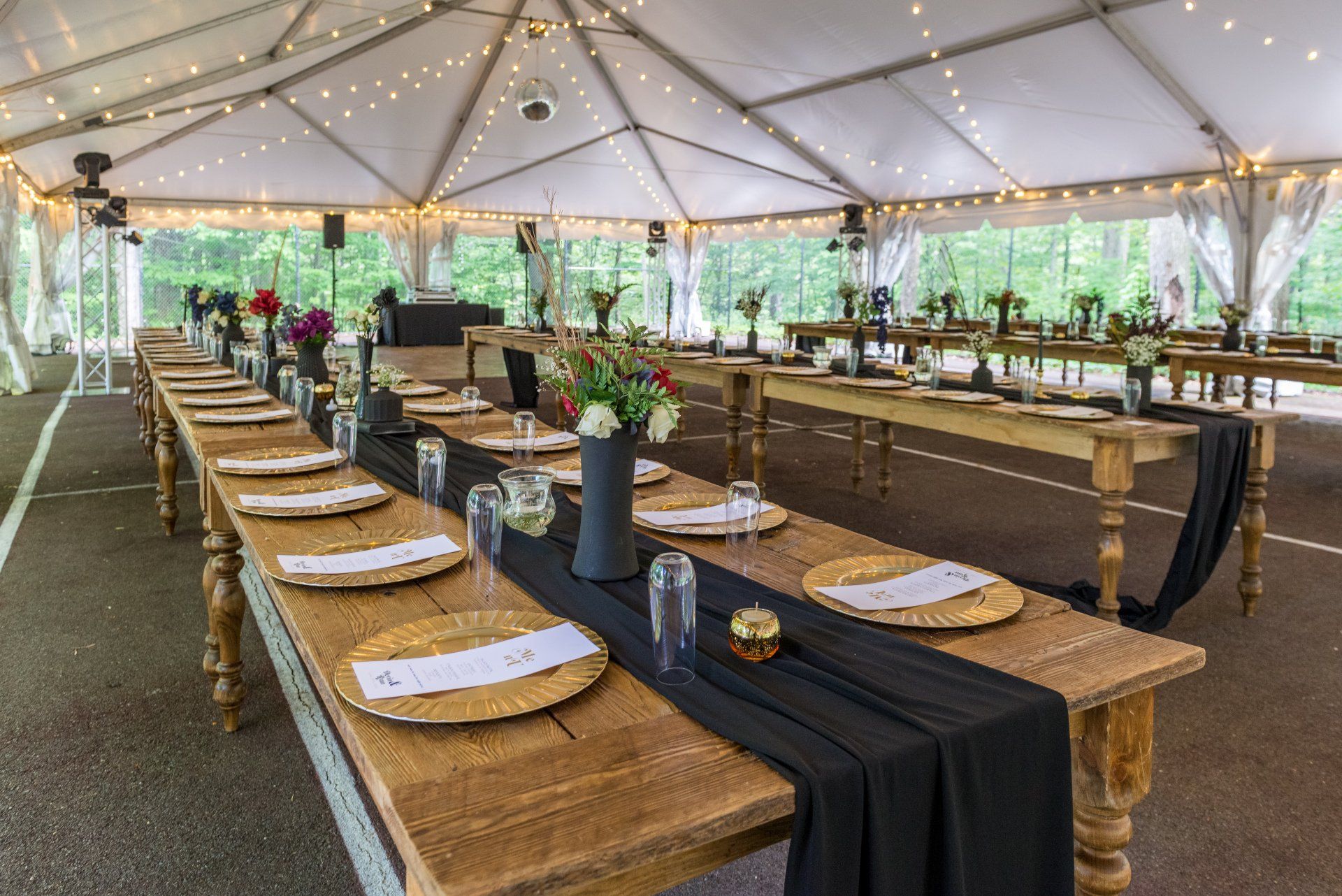 A long wooden table with plates and glasses on it under a tent.