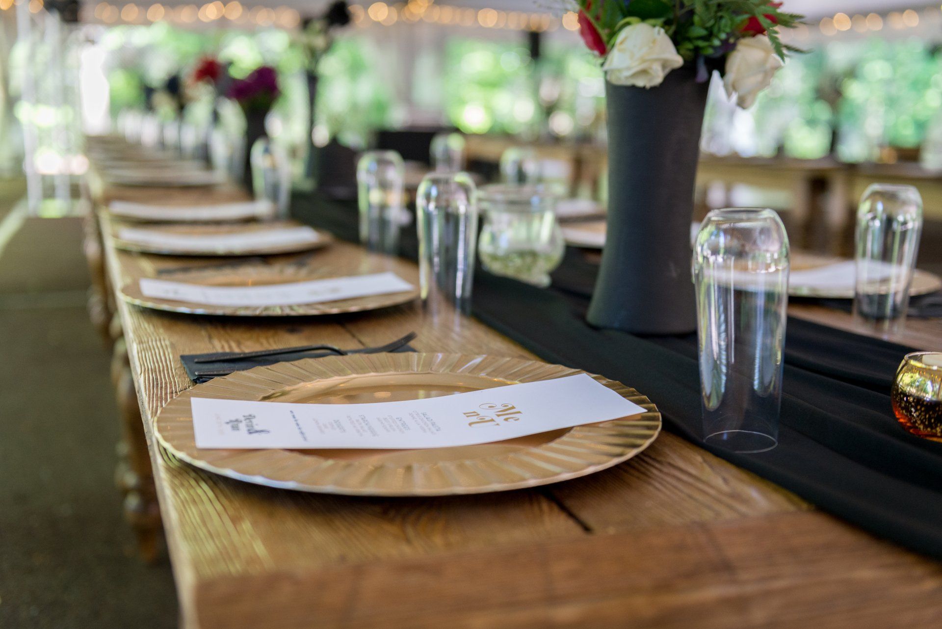 A long wooden table with plates , glasses , and a vase of flowers.
