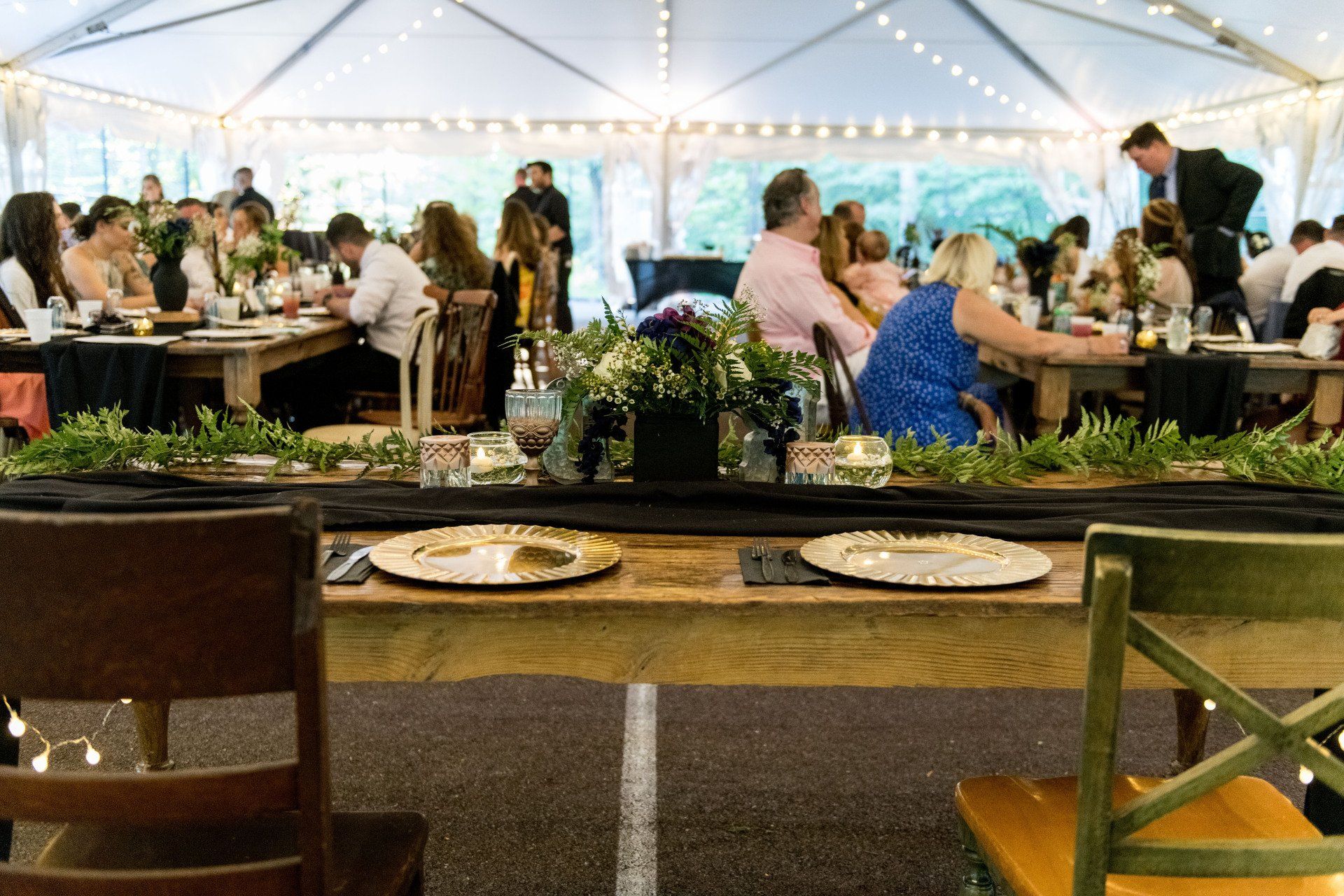 A group of people are sitting at tables under a tent at a wedding reception.