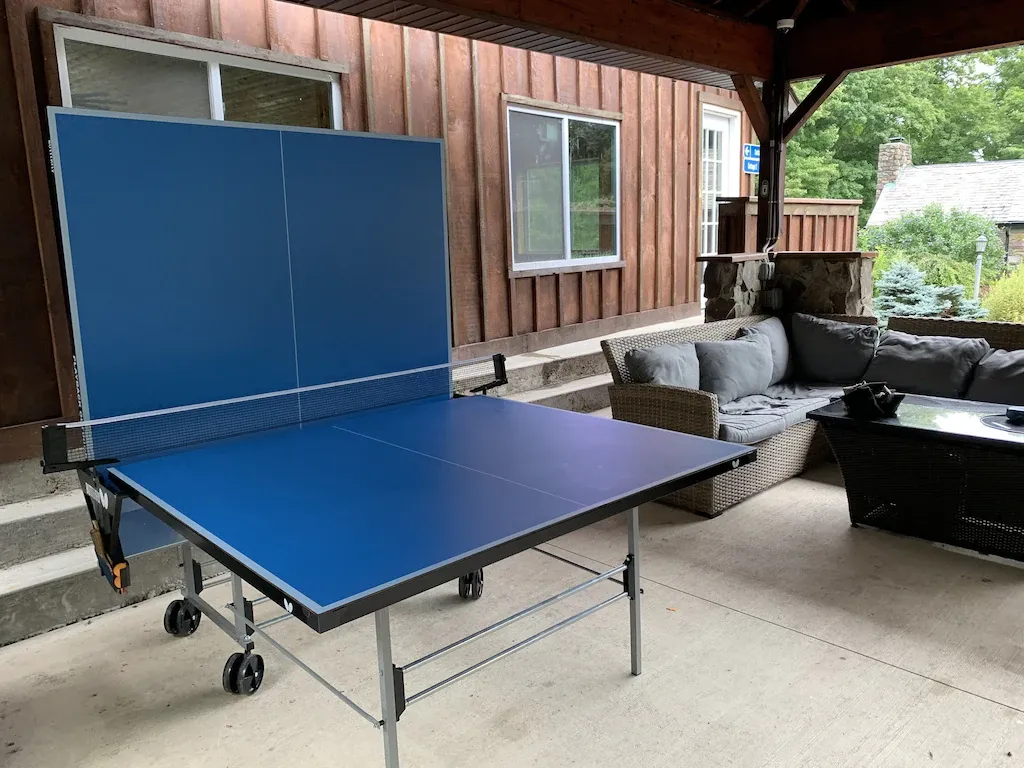 A blue ping pong table is sitting on a patio next to a couch.