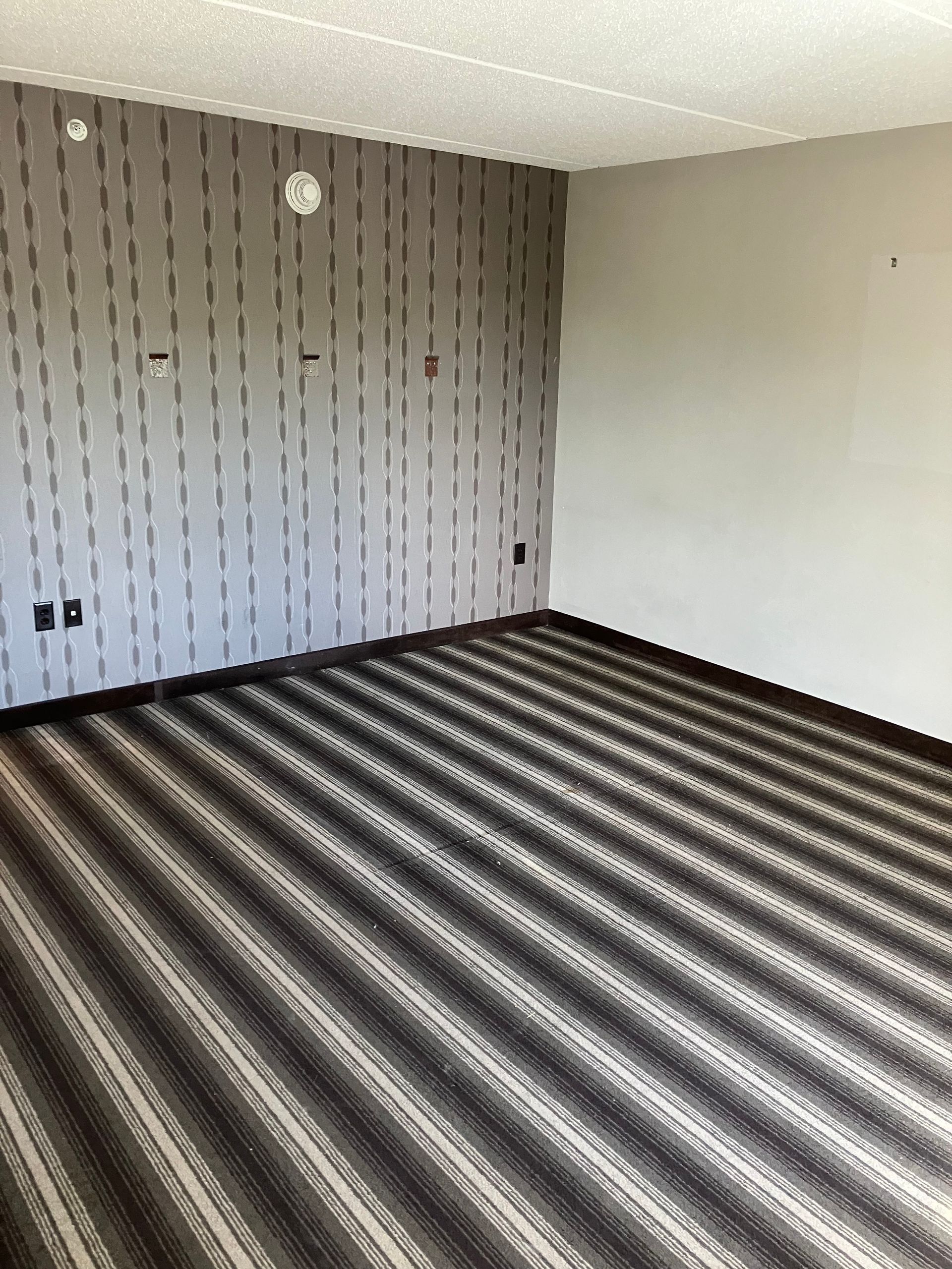 Empty room with patterned carpet and vertical-striped accent wall.