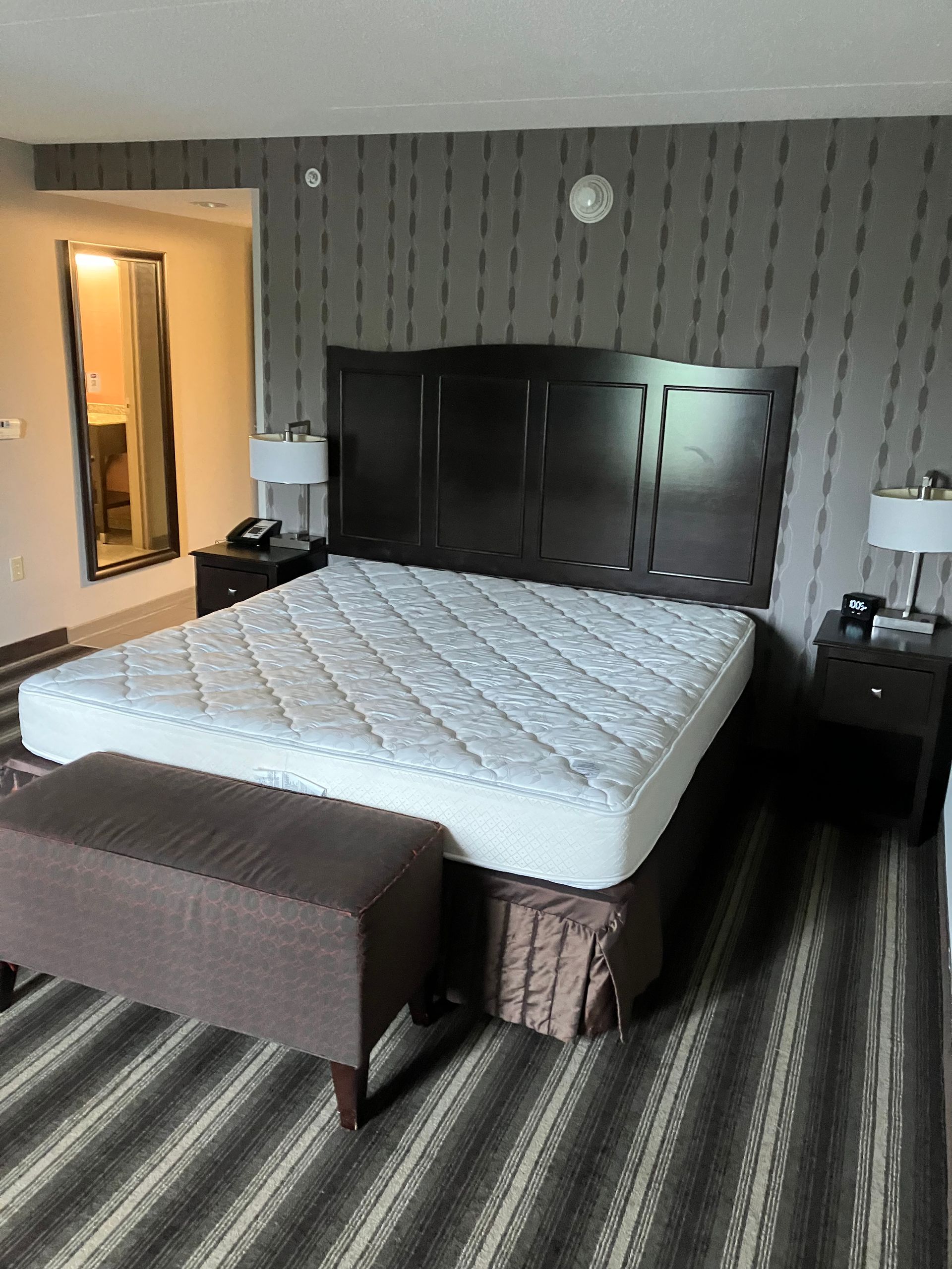 A hotel room with a bed, nightstands, lamps, and patterned wallpaper.