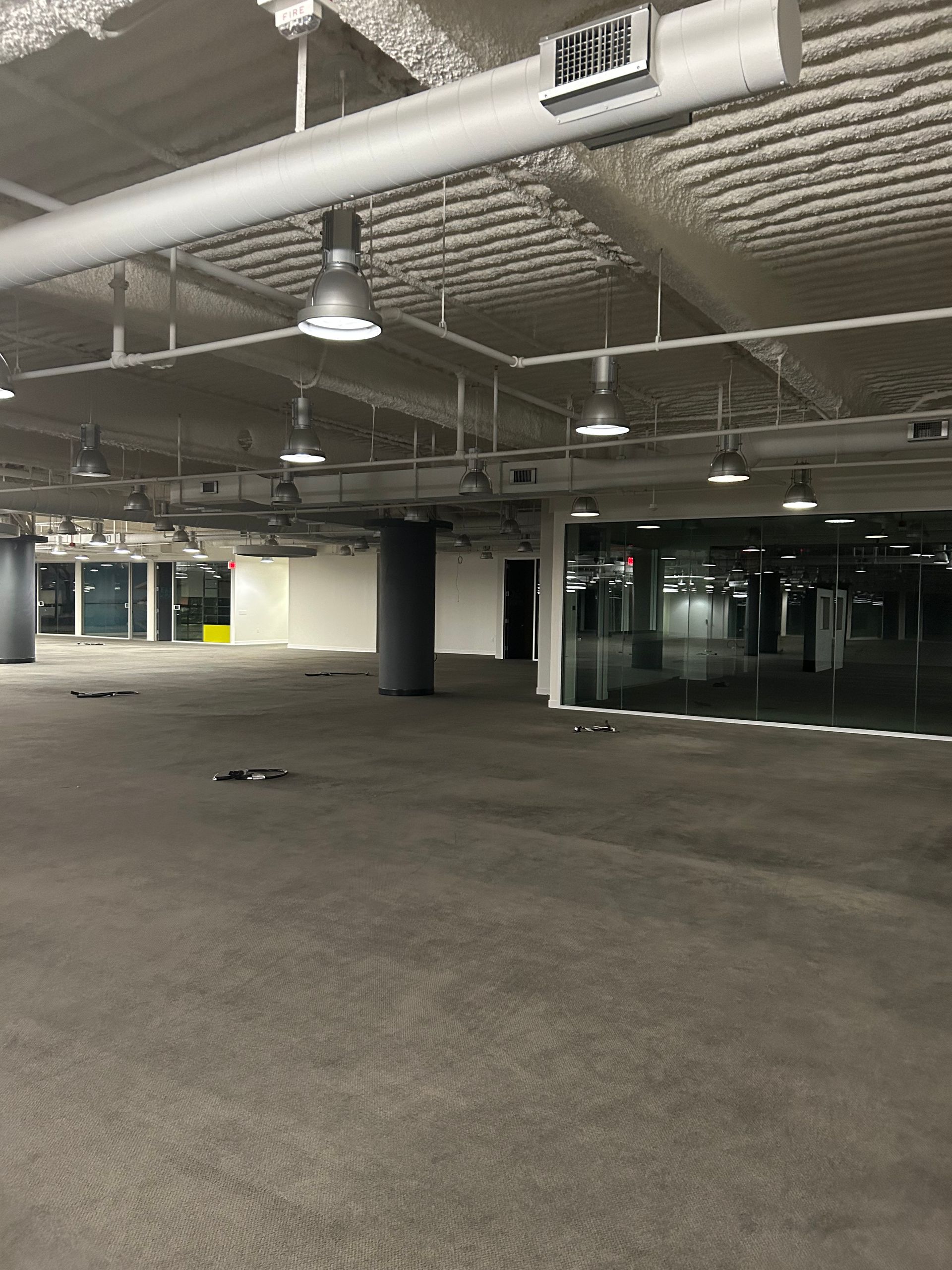 An empty modern office space with gray carpet, large windows, and exposed ceiling fixtures.