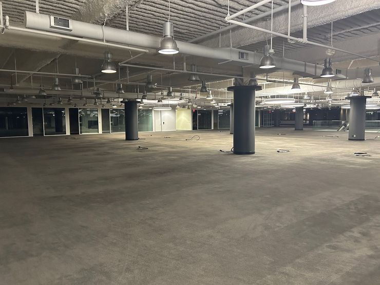 Empty, vast commercial space with gray carpet, pillars, and overhead lighting.