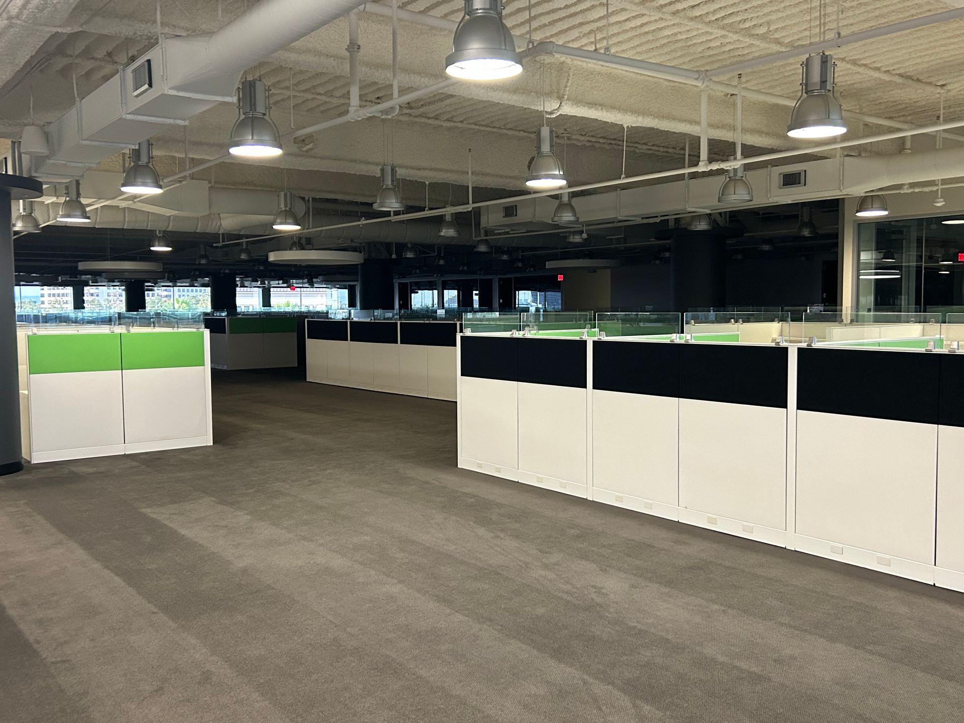 Empty office cubicles, white and black panels, green accents, fluorescent lighting.