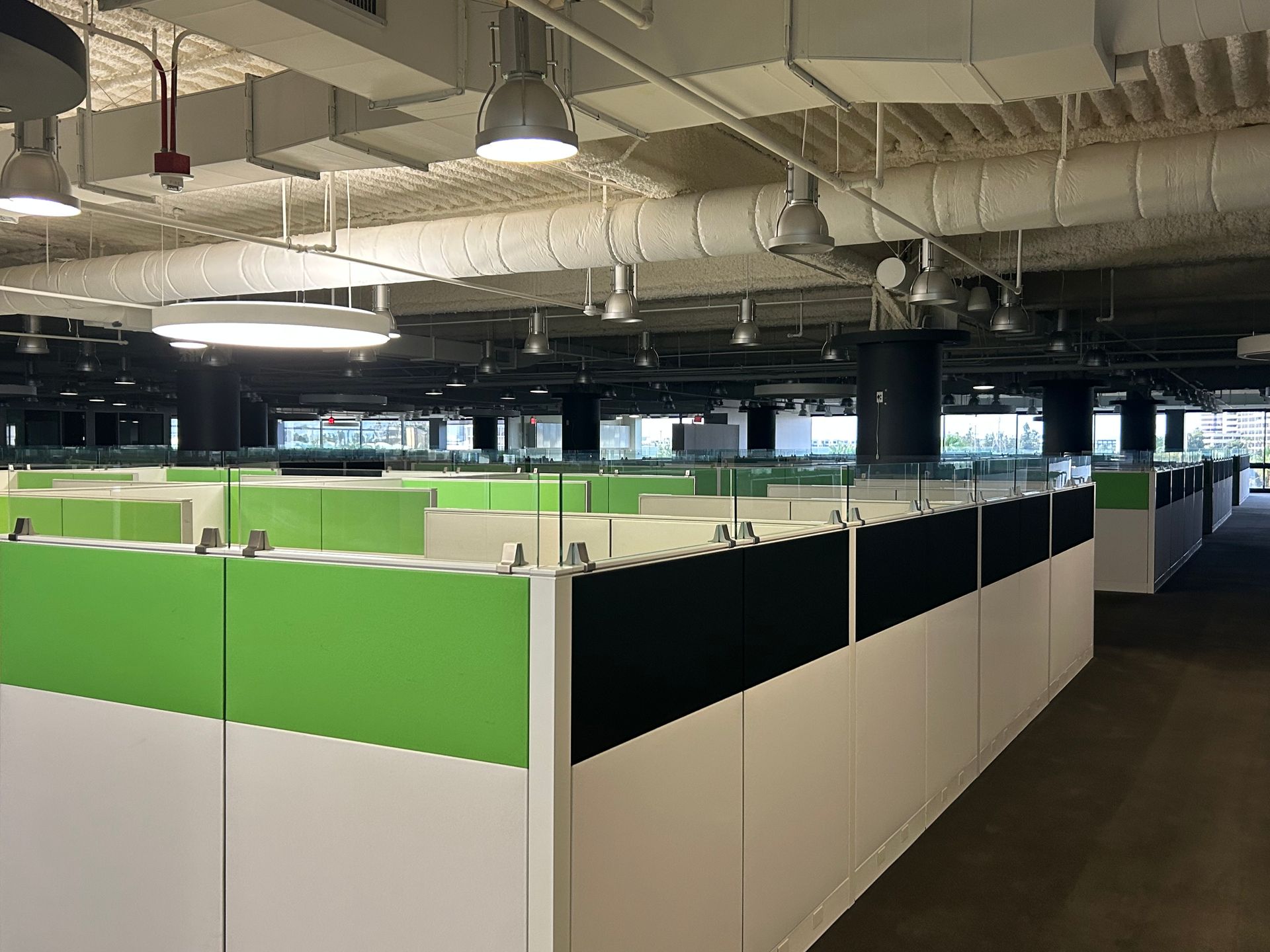 Cubicle office space with green, black, and white partitions under exposed ceiling.