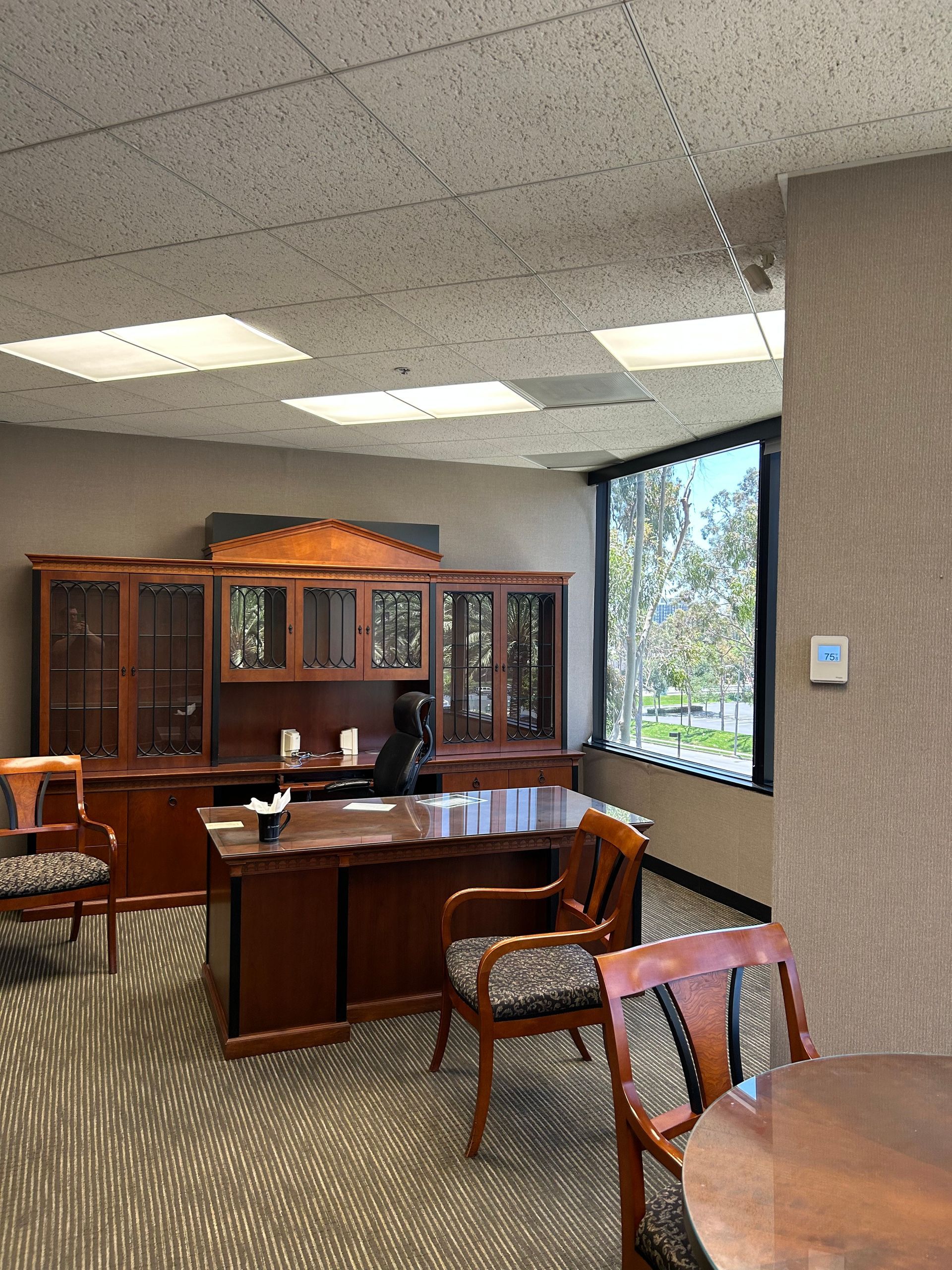 Office with wooden desk, chairs, and cabinet. A window offers a view outside.