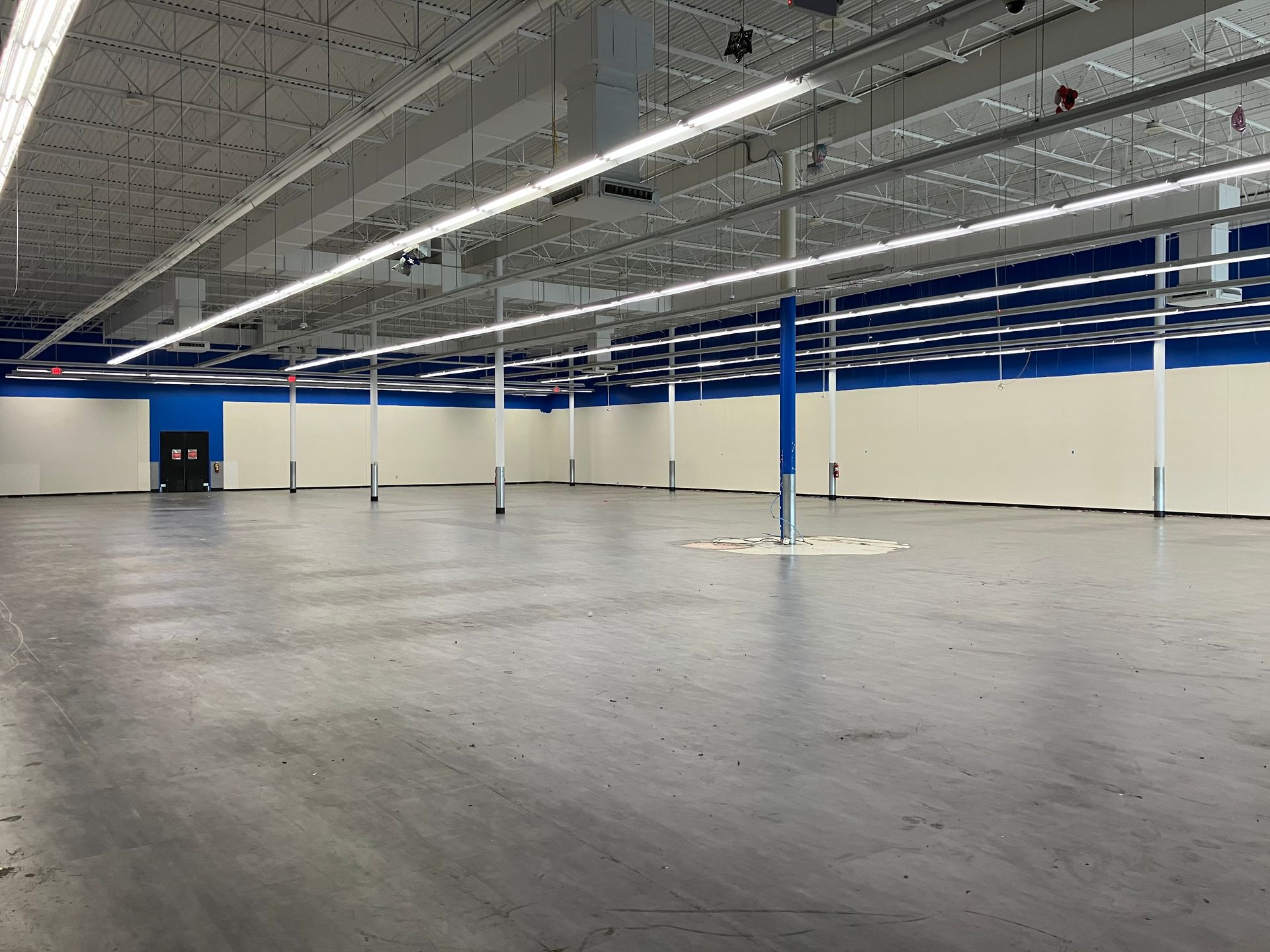 Empty retail space with gray floor, white walls with blue trim, and exposed ceiling.
