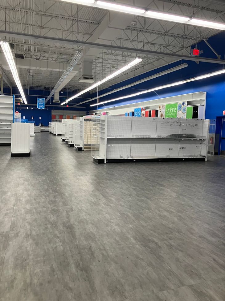 Empty store interior with rows of shelves, blue walls, and gray floor.