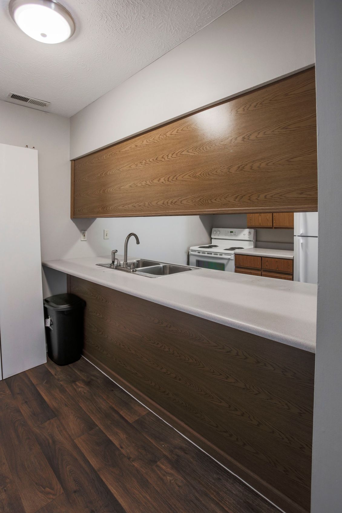 a kitchen with a sink , stove , refrigerator and trash can .