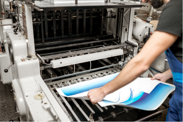 Person loading printed sheets into an industrial printing press with blue gradient design.