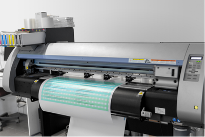 Large-format printer producing a cyan banner with paper feeding through the machine