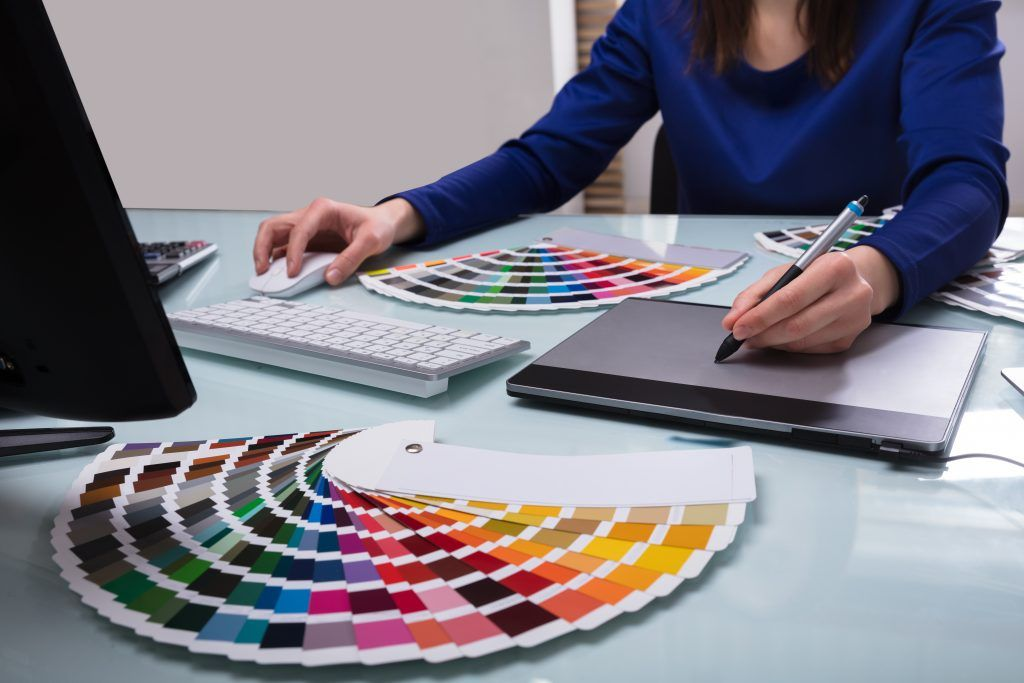 Person using a mouse and stylus on a design tablet, with color swatches on a desk.