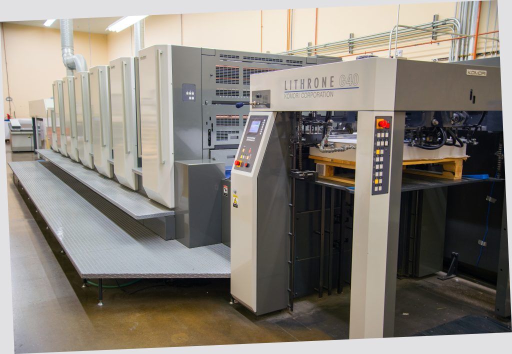 Large printing press in a warehouse setting, with paper pallets loaded, ready to print.