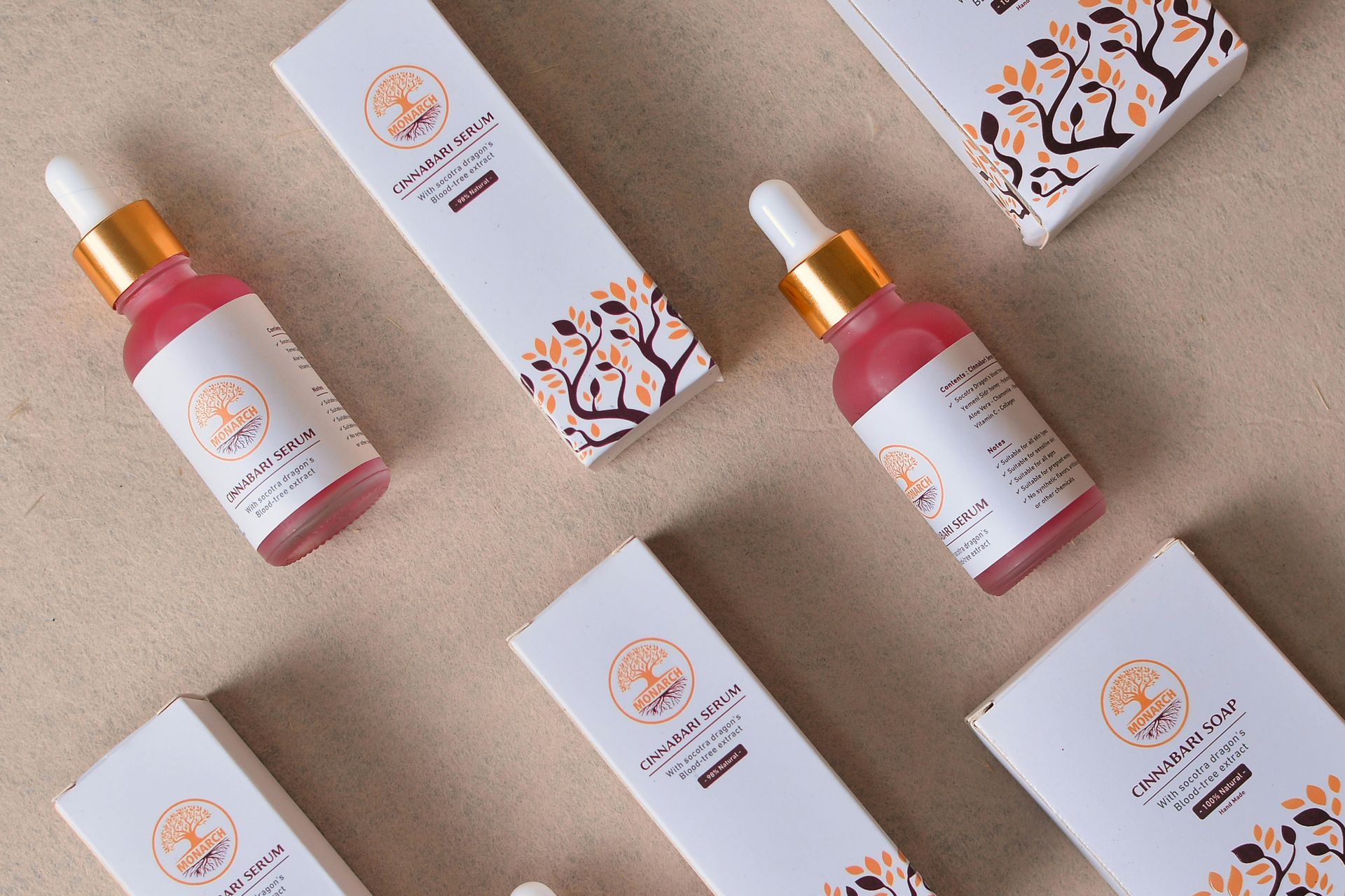 Bottles of pink liquid with dropper tops, and white boxes with floral design on beige surface.