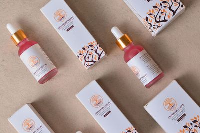 Pink skincare bottles and white boxes arranged diagonally on a beige surface