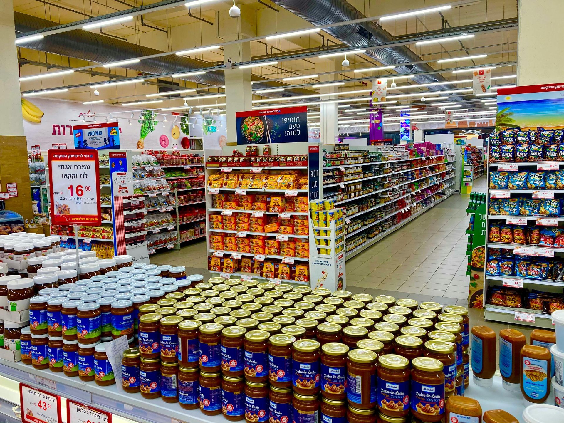 Supermarket interior with rows of stocked shelves, displays of food products, and bright overhead lighting.