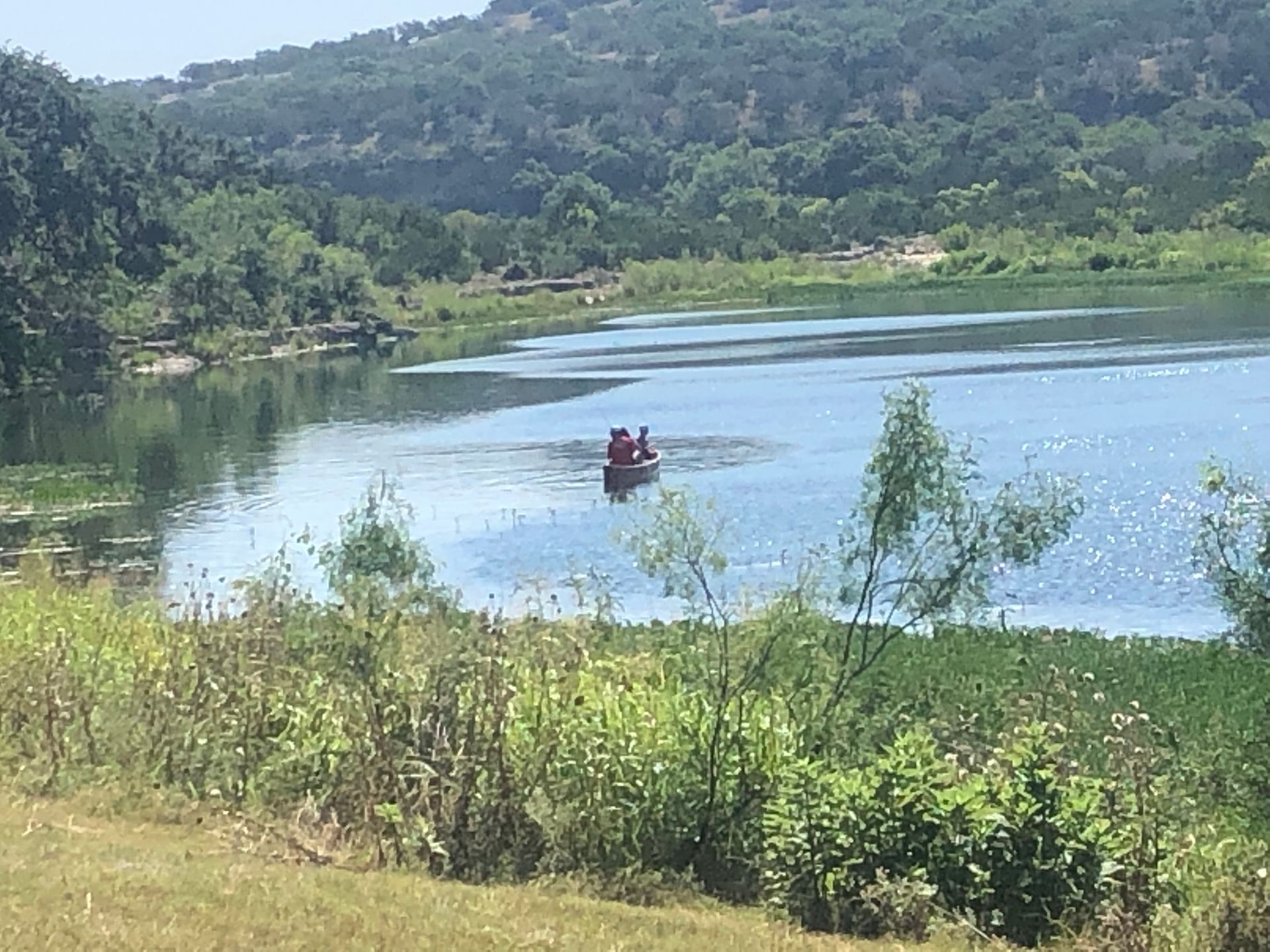 A canoe with two people on a lake, surrounded by trees and green vegetation.