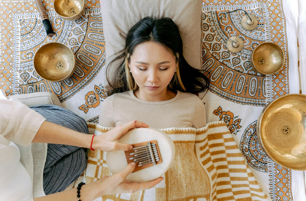 A woman is laying on a blanket with a bowl on her head.