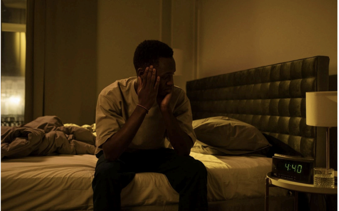 A man is sitting on a bed with his hands on his face.