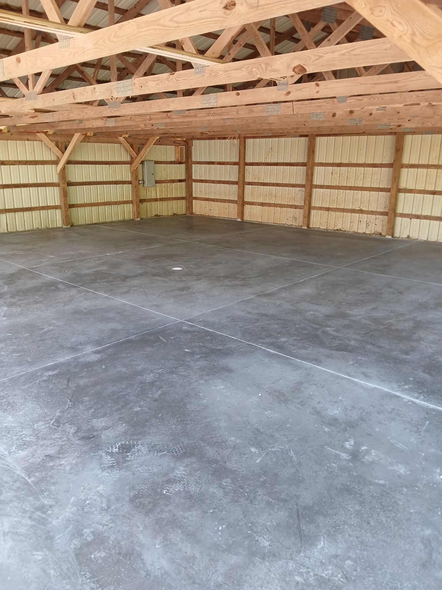 An unfinished building interior featuring a concrete floor, exposed wooden ceiling trusses, and spray-foam insulated walls.