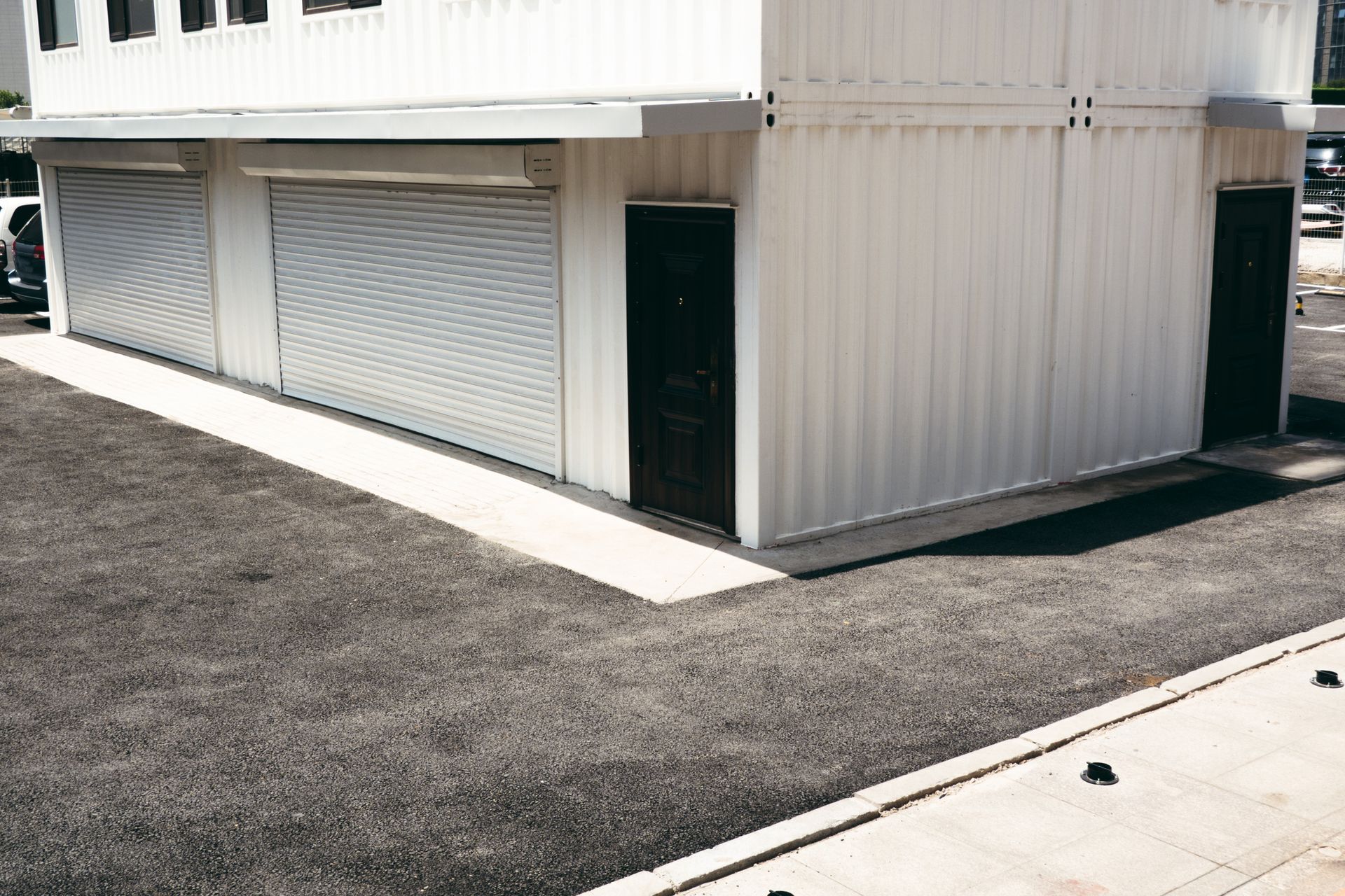 A white building with a black door and roller shutters