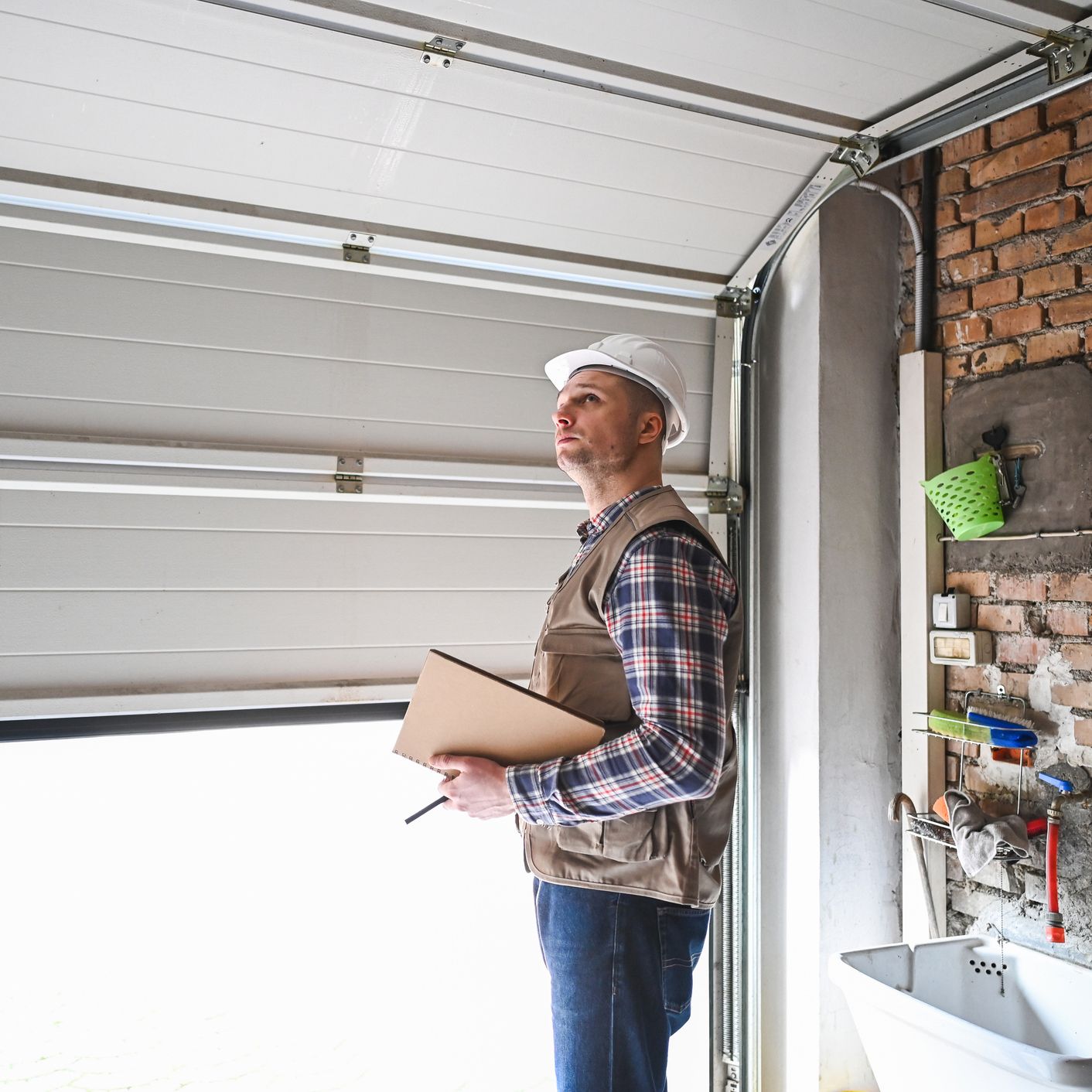 A man is standing in front of a garage door holding a clipboard.