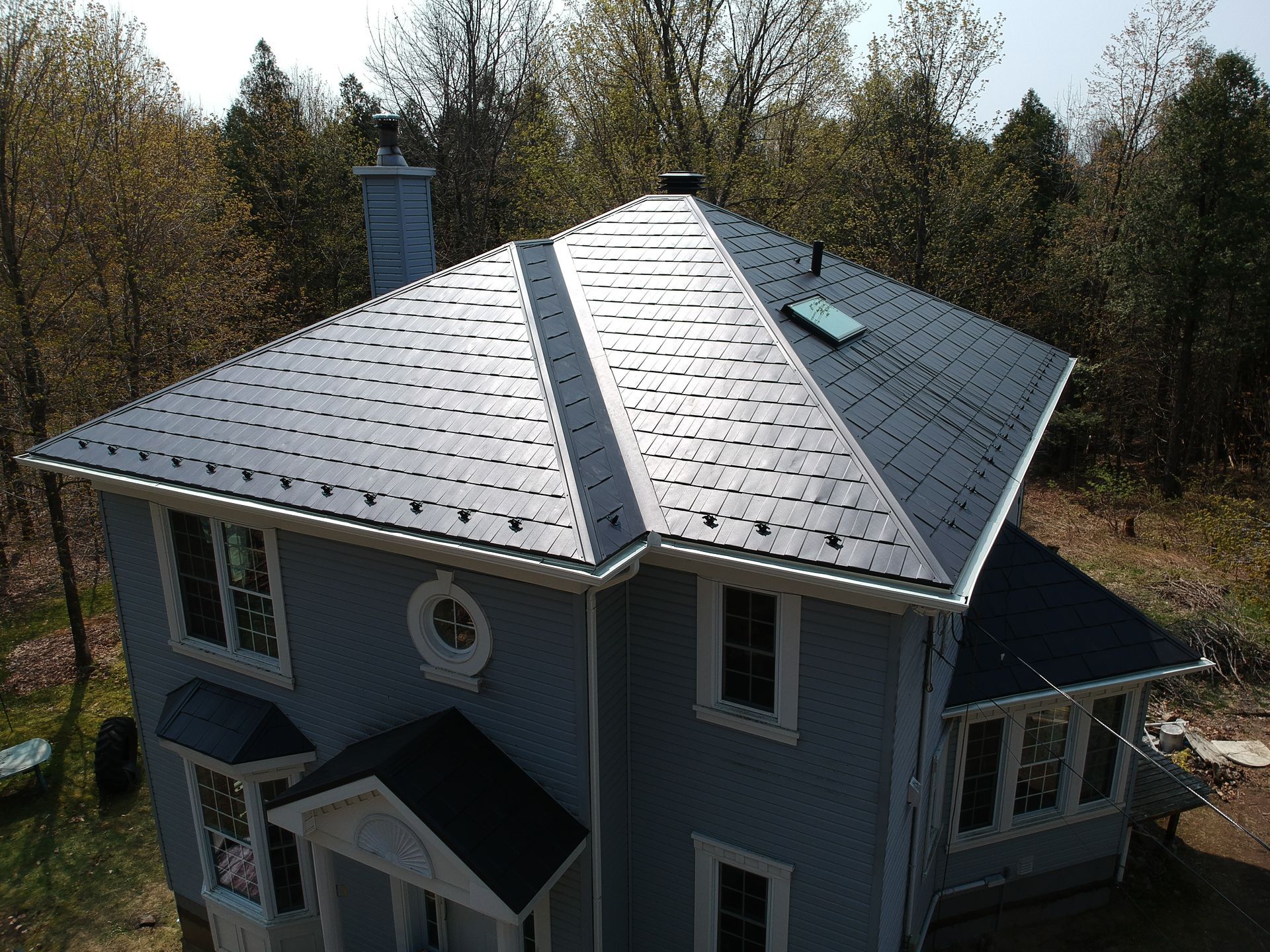 An aerial view of a blue house with a black roof surrounded by trees.