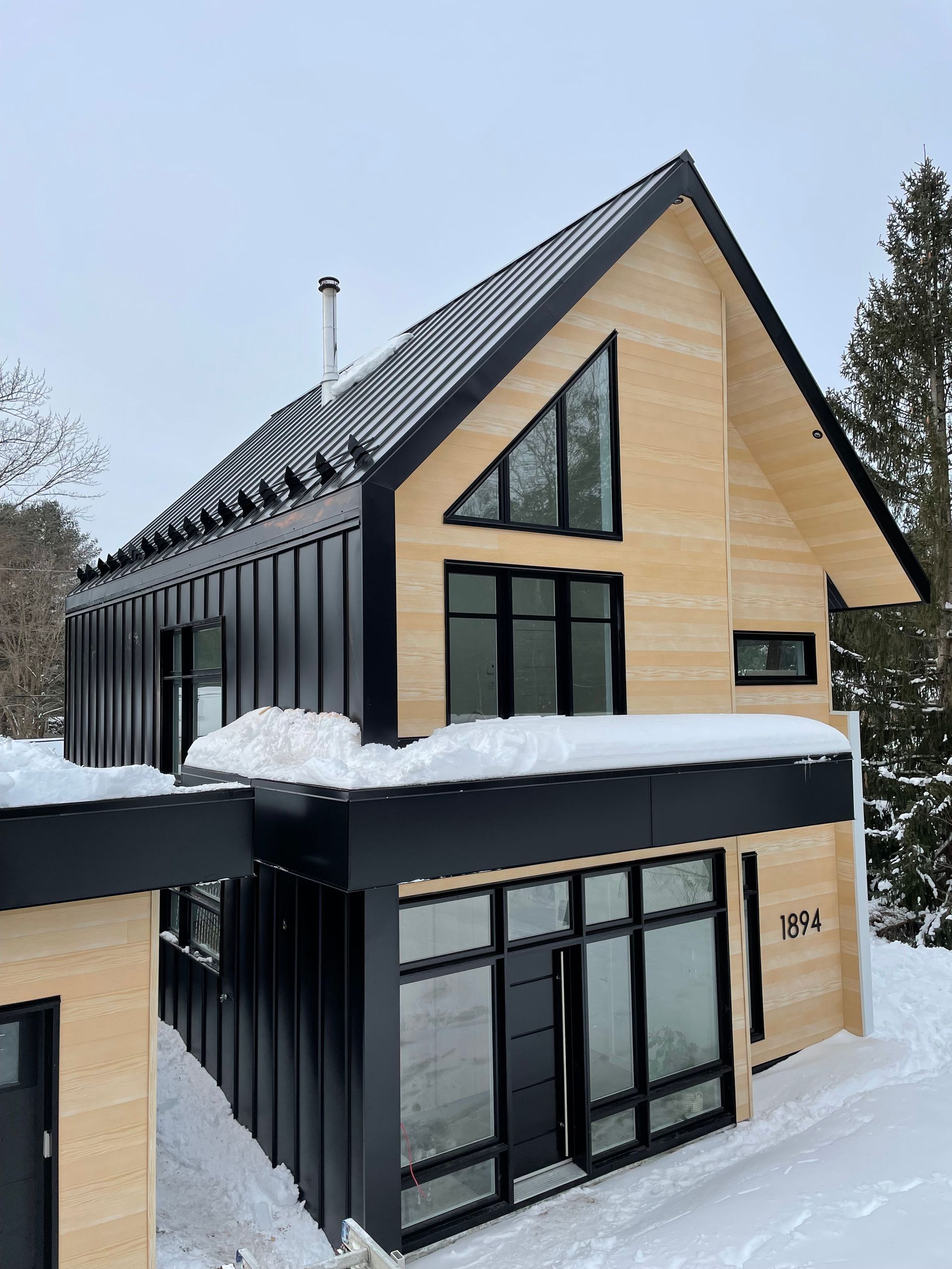 Une maison avec un toit noir et beaucoup de fenêtres est recouverte de neige.