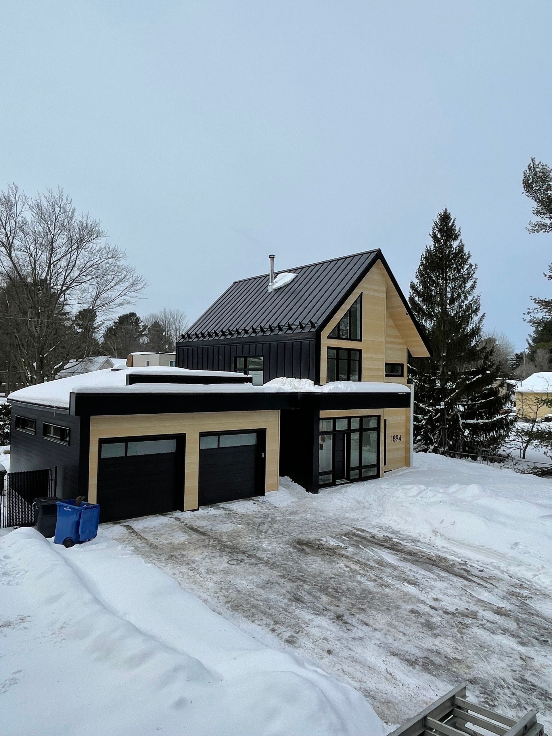 Une maison avec un toit noir et un garage est recouvert de neige.
