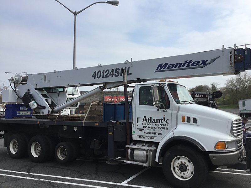 A white Atlantic Crane truck with a raised Manitex crane on a city street.