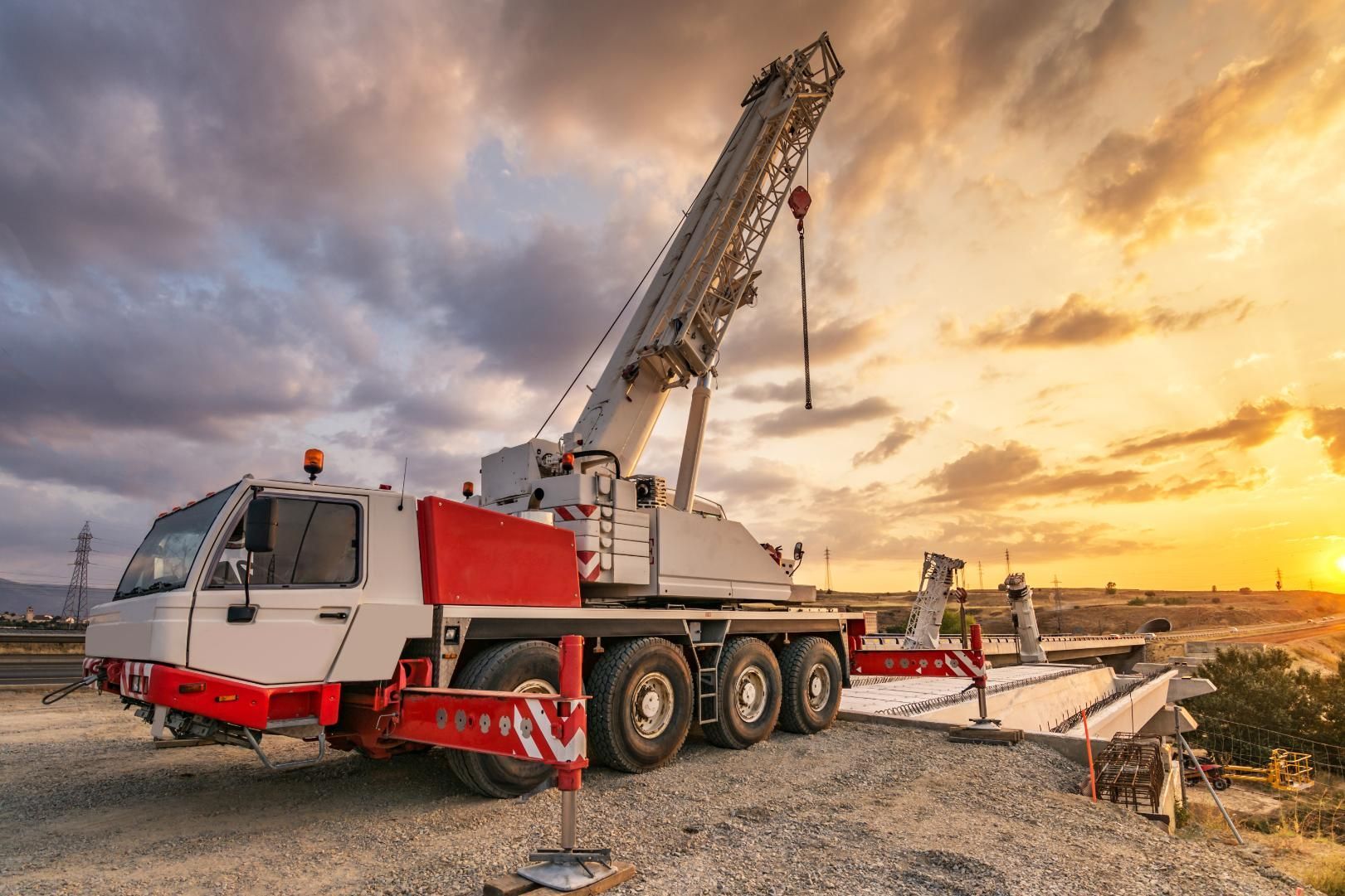 Mobile crane on a construction site with an elevated boom against a sunset.