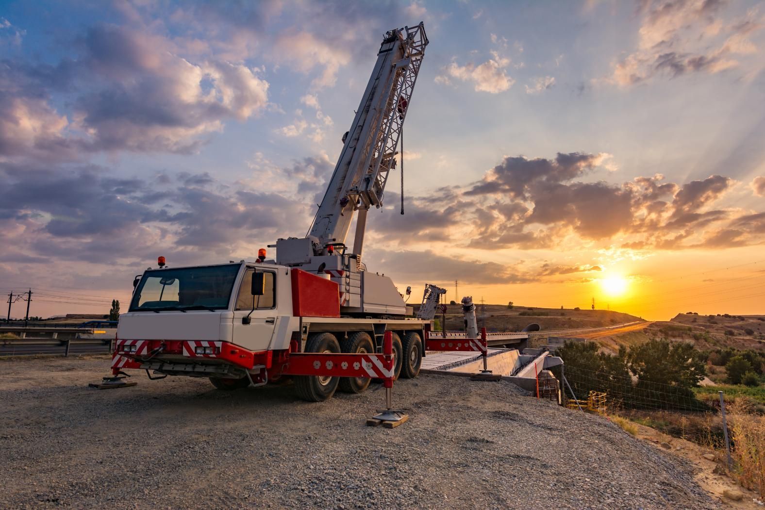 Mobile crane on a construction site at sunset, with a vibrant orange sky.