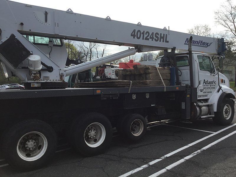 Crane truck transporting stone blocks on a flatbed, parked on asphalt.
