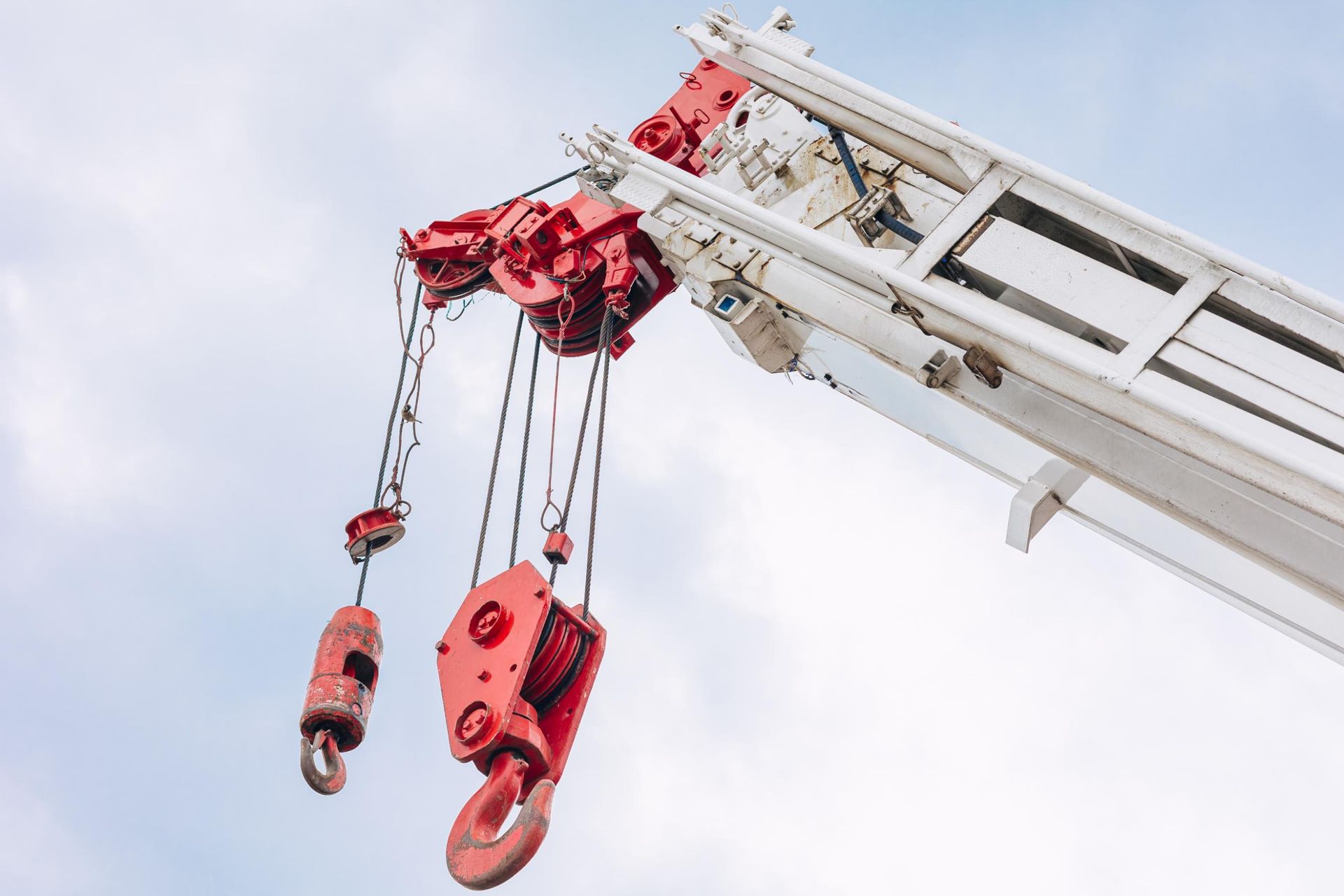 Red and white crane arm with multiple hooks, against a cloudy sky.