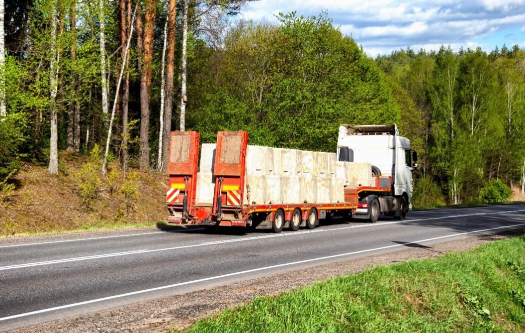 Truck carrying large cargo on a road, trees in the background.