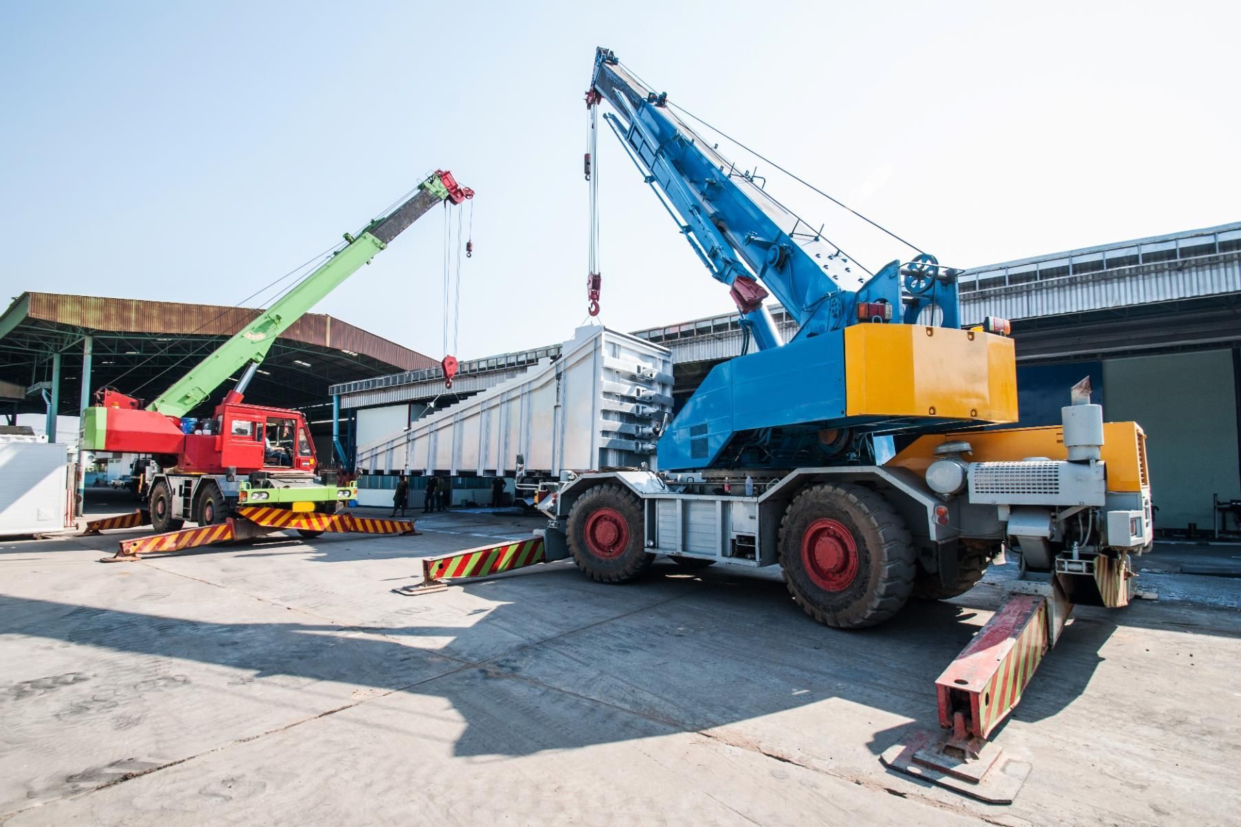 Two mobile cranes lifting a trailer in a sunny outdoor setting.