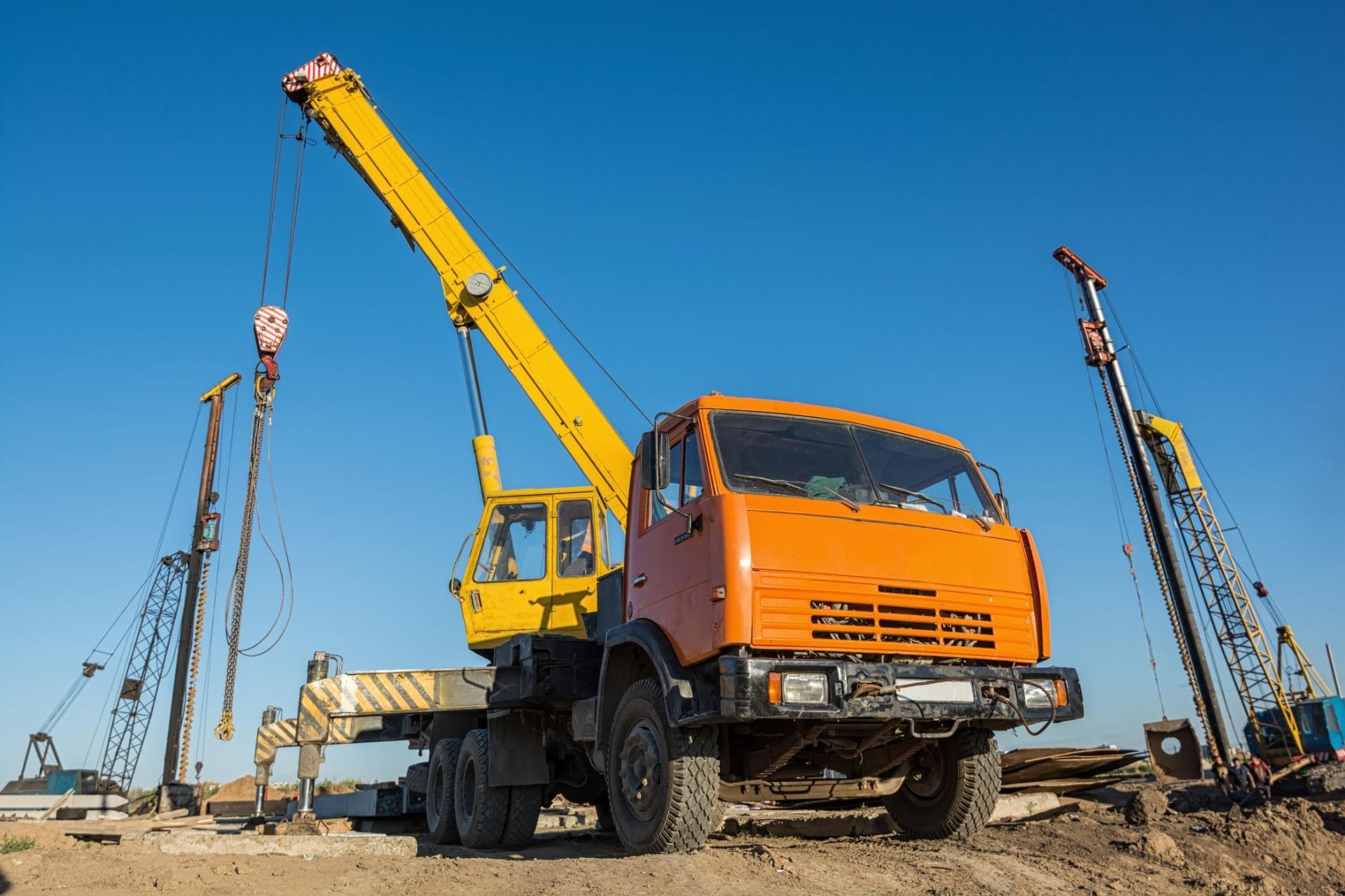 Orange crane truck on a construction site with yellow boom against a clear blue sky.
