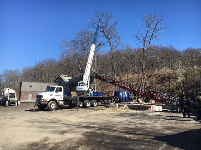 A crane next to a rock crushing machine, with a truck and conveyor belt. Blue sky.