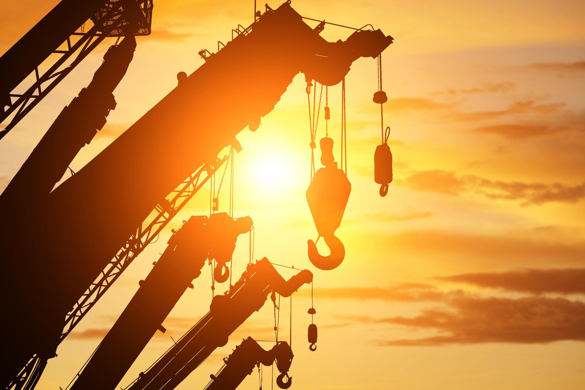 Silhouette of cranes with hooks against a bright orange sunset.