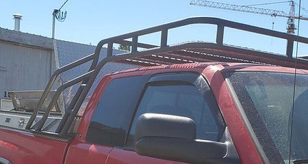 Red pickup truck with a black roof rack parked outdoors near a building under blue sky