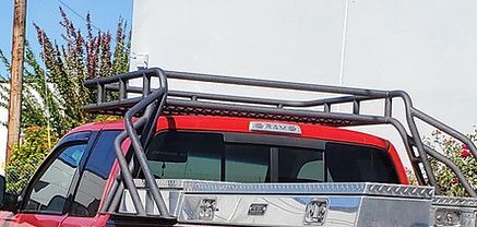 Red pickup truck with a black bed rack parked outdoors near plants