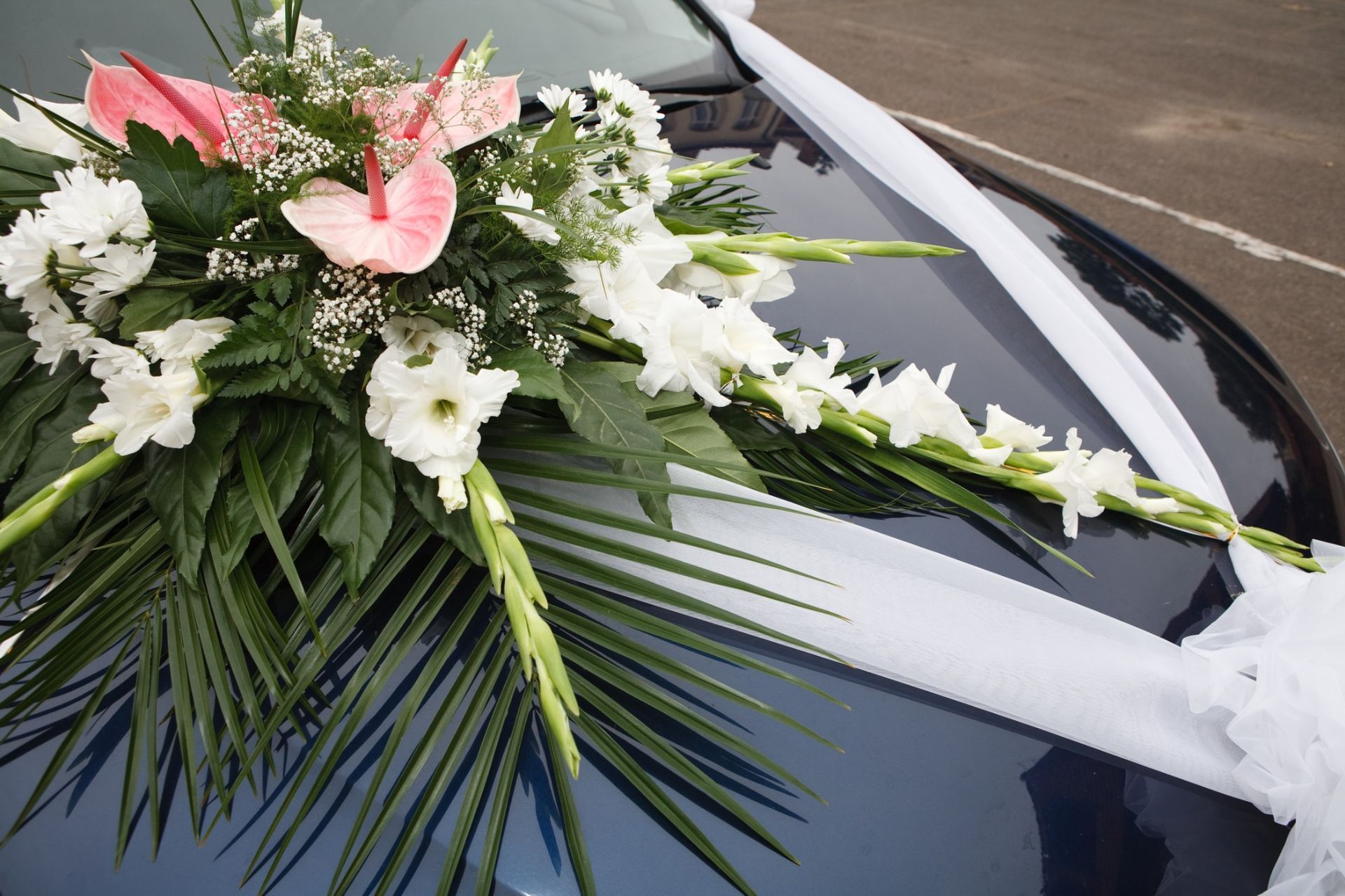 A car with flowers on the hood is decorated for a wedding.