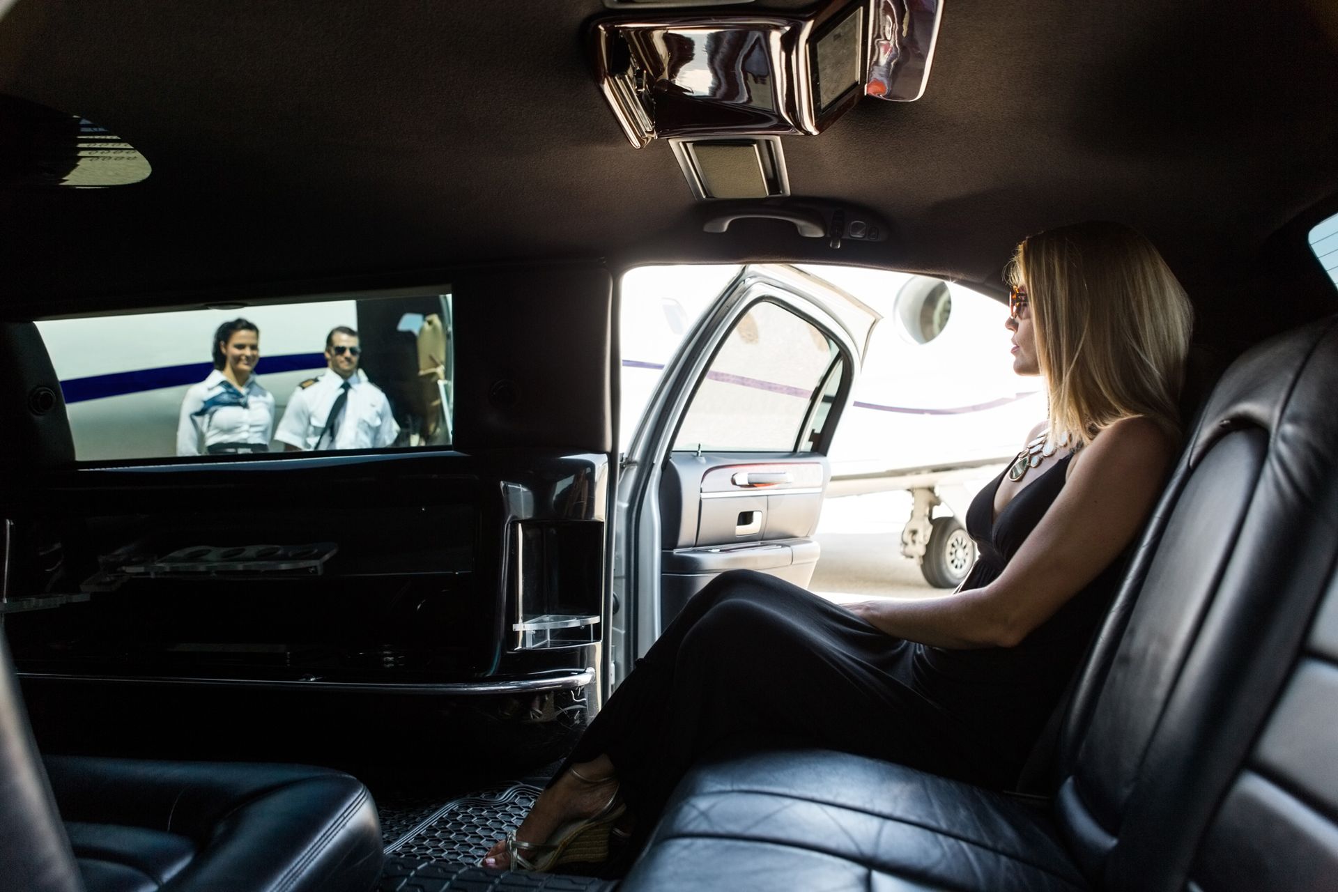 A woman is sitting in the back seat of a limousine watching a movie.