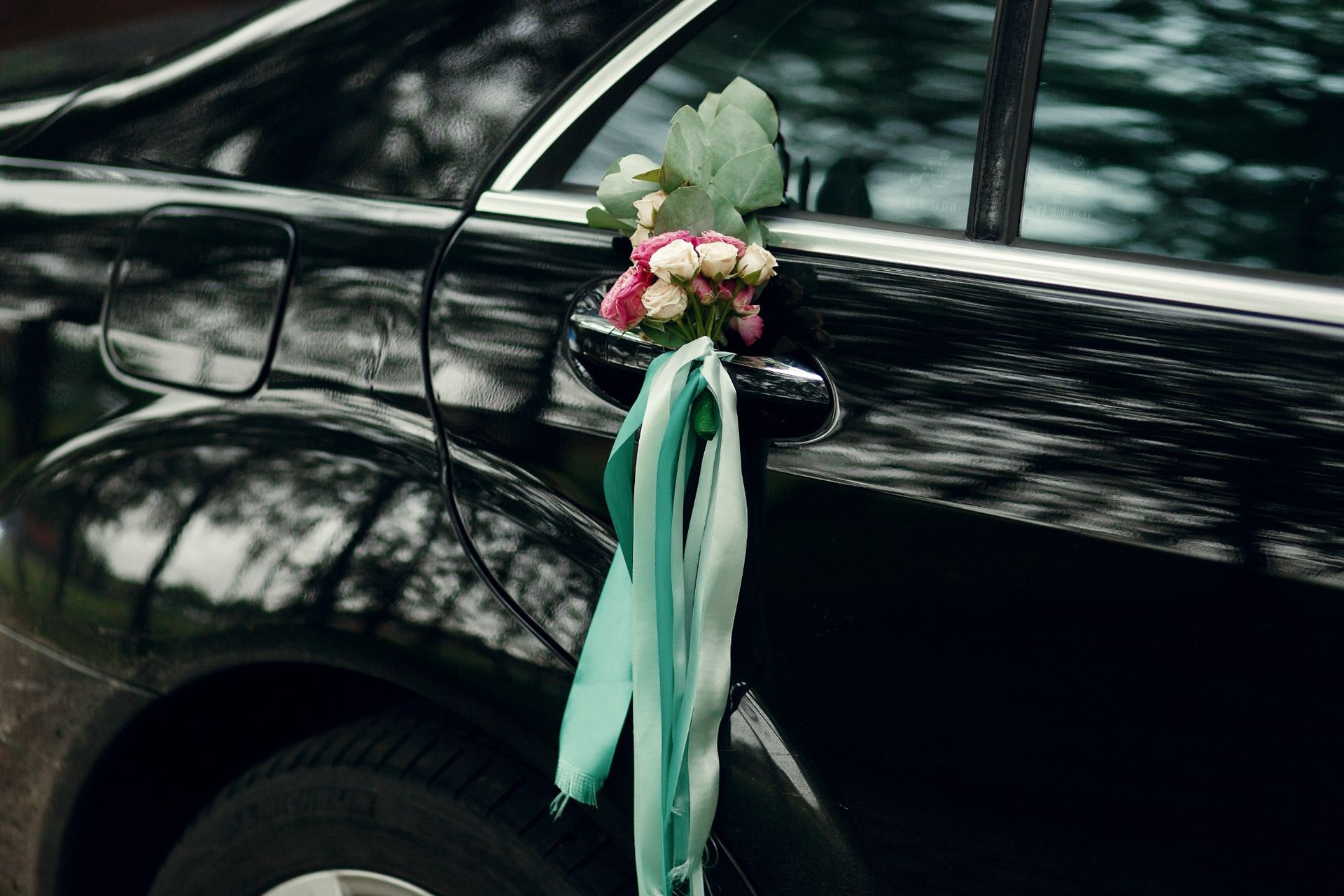 A black wedding car decorated with flowers and ribbons.