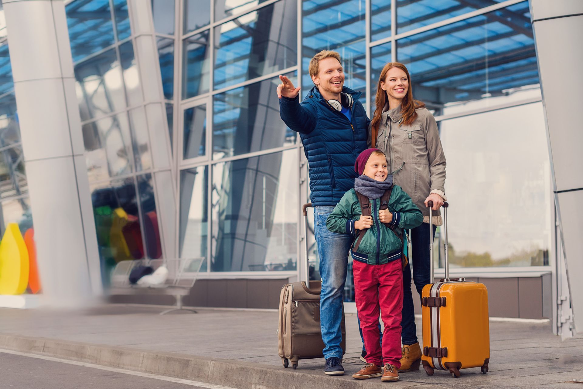 A family with luggage is standing in front of an airport.