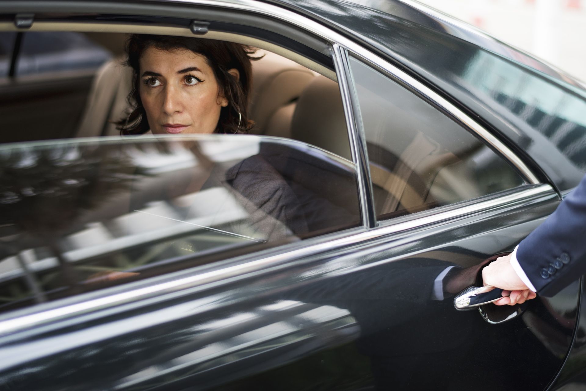 A woman is sitting in the back seat of a car while a man opens the door.